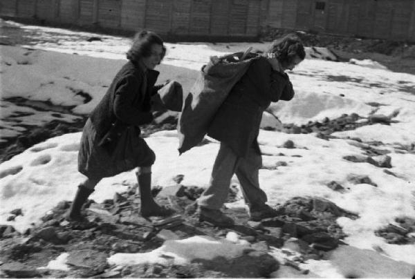 Italia Dopoguerra. Milano - Quartiere Baggio - Coppia di giovani ragazze tra gli edifici prefabbricati in costruzione trasporta un sacco di materiale vario