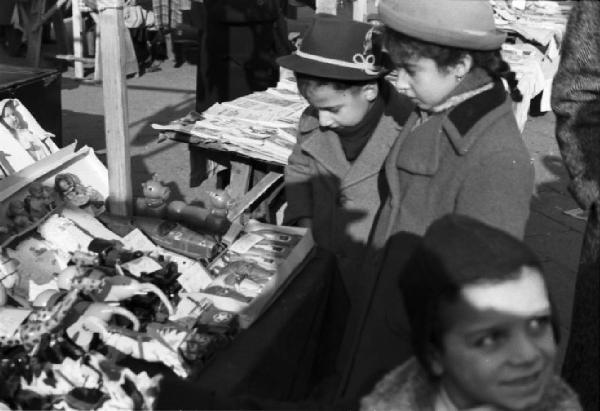 Italia Dopoguerra. Milano - fiera degli Obèi - Obèi: scorcio tra un gruppo di bambini fermi davanti a una bacarella di giocattoli