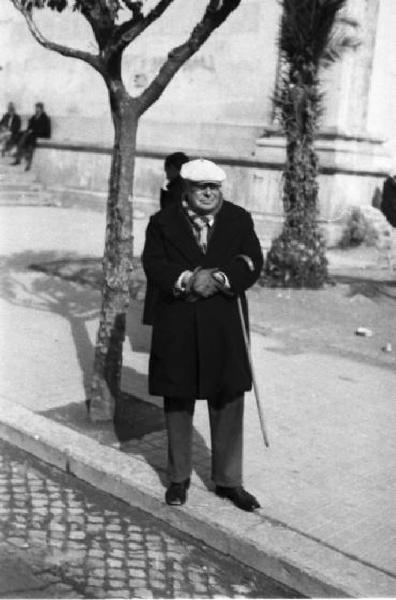 Italia Dopoguerra. Terracina. Un uomo anziano con cappello e bastone in attesa lungo un viale