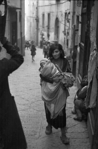 Italia Dopoguerra. Napoli. Una donna cammina per le vie della città reggendo un bambino avvolto in una coperta