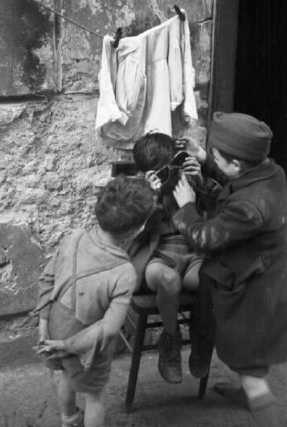 Italia Dopoguerra. Napoli. Tre bambini giocano con un paio di occhiali sull'uscio di un'abitazione