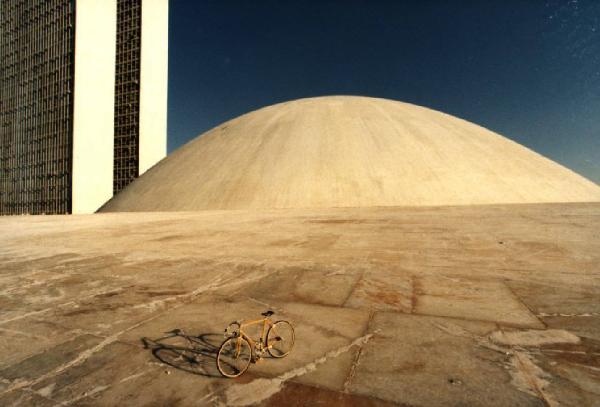 Brasilia. Bicicletta da corsa davanti a una delle due cupole del Congresso Nazionale, con la base del doppio grattacielo sullo sfondo