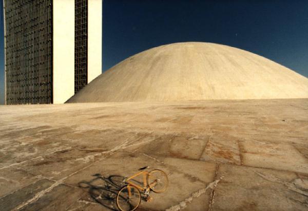 Brasilia. Bicicletta da corsa davanti a una delle due cupole del Congresso Nazionale, con la base del doppio grattacielo sullo sfondo