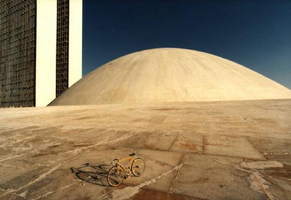 Brasilia. Bicicletta da corsa davanti a una delle due cupole del Congresso Nazionale, con la base del doppio grattacielo sullo sfondo