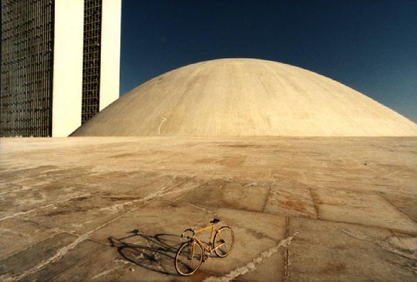 Brasilia. Bicicletta da corsa davanti a una delle due cupole del Congresso Nazionale, con la base del doppio grattacielo sullo sfondo