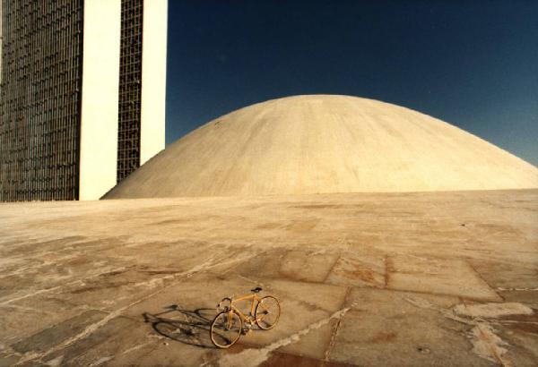 Brasilia. Bicicletta da corsa davanti a una delle due cupole del Congresso Nazionale, con la base del doppio grattacielo sullo sfondo