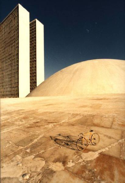 Brasilia. Bicicletta da corsa davanti a una delle due cupole del Congresso Nazionale, con la base del doppio grattacielo sullo sfondo