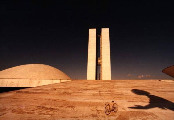 Brasilia. Bicicletta da corsa davanti al doppio grattacielo del Congresso Nazionale. Si nota un'ombra di persona sulla spianata lastricata