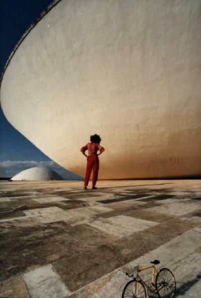 Brasilia. Bicicletta da corsa e figura femminile (Cyssa) davanti a una cupola del Congresso Nazionale, con l'altra sullo sfondo