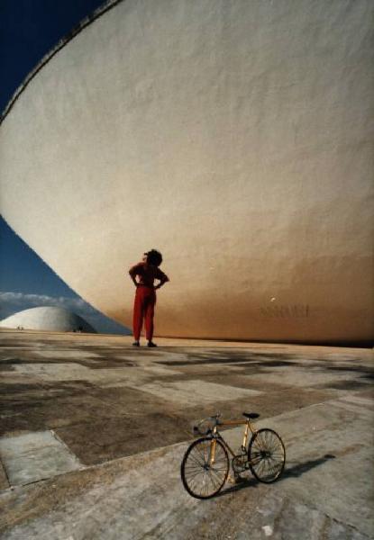 Brasilia. Bicicletta da corsa e figura femminile (Cyssa) davanti a una cupola del Congresso Nazionale, con l'altra sullo sfondo