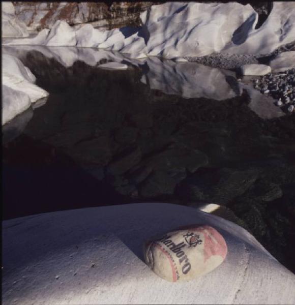 Marlboro. Sasso dipinto come il pacchetto di sigarette appoggiato sulle rocce accanto a un corso d'acqua