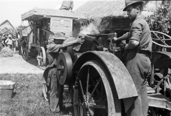 Inzago. Trebbiatura. Addetti alla manutenzione forniscono di carburante i macchinari - sullo sfondo contadini alle prese con una trebbiatrice