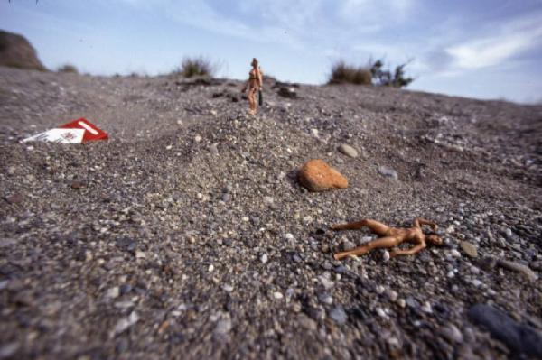 Marlboro. Pacchetto di sigarette con piccola bambole nude in pose da modelle, su cumulo di ghiaia