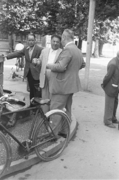 Milano. Parco Sempione. Tre persone discutono attorno alla "Fontana dell'acqua marcia" - uno regge unbicchiere d'acqua