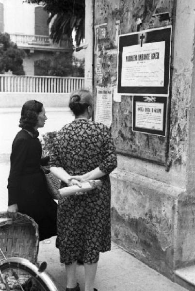 Diano Marina. Due donne del paese leggono annunci mortuari affissi ai muri