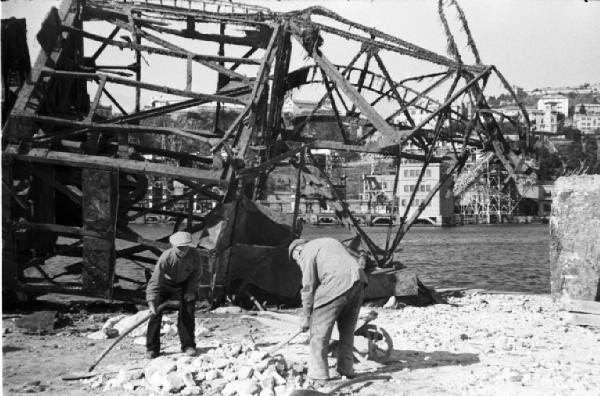 Italia Dopoguerra. Savona. Porto. Operai sgomberano il terreno dalle macerie - sullo sfondo strutture industriali metalliche abbattute