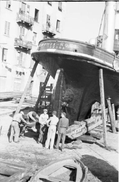 Savona. Porto. Poppa della nave Mari Noli in secca sulla banchina del porto - operai al lavoro - sullo sfondo una palazzina per abitazioni