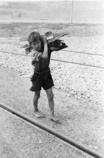 Porto Marghera. Bambino porta assi di legno sulle spalle, camminando lungo dei binari