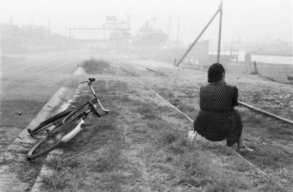 Porto Marghera. Una donna siede lungo i binari del porto a lato di una bicicletta