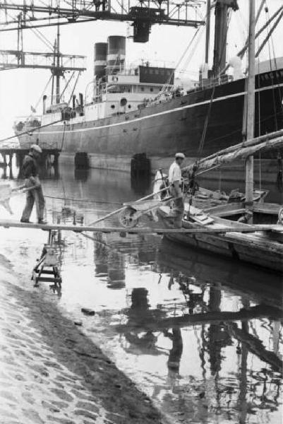 Porto Marghera. Operai compiono operazioni di carico, una nave è ormeggiata sullo sfondo