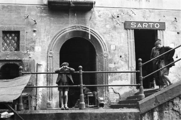 Italia Dopoguerra. Napoli. Un bambino in prossimità di un negozio da sarto si sporge da una balaustra guardando verso il basso