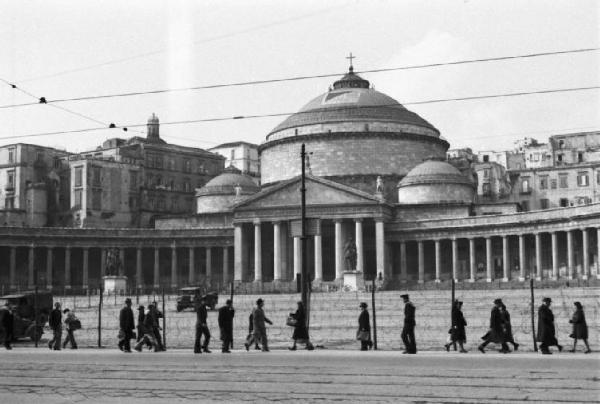 Italia Dopoguerra. Napoli. Basilica recintata con filo spinato e presidiata da militari. Persone camminano lungo la strada