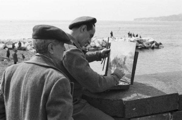 Italia Dopoguerra. Napoli. Un pittore sul lungomare dipinge un paesaggio, un passante guarda