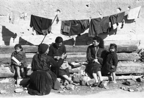 Italia Dopoguerra. Terracina. Gruppo di donne e bambine sedute su tronchi parlano