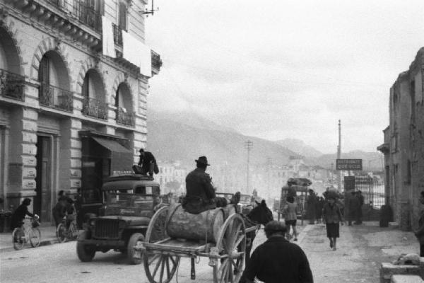 Italia Dopoguerra. Formia. Automobili, carretti e biciclette lungo una via