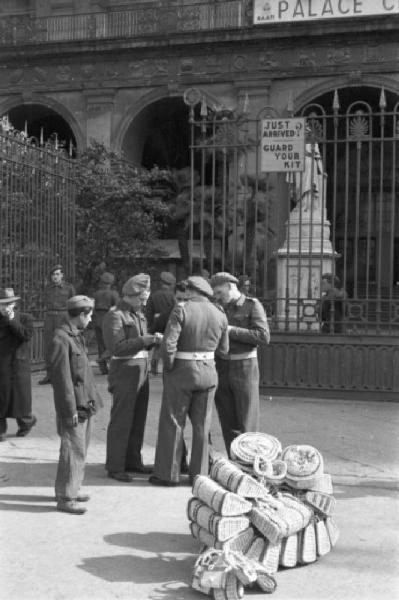 Italia Dopoguerra. Napoli. Gruppo di militari in prossimità di Palazzo Reale. Mucchi di borse e cesti in paglia