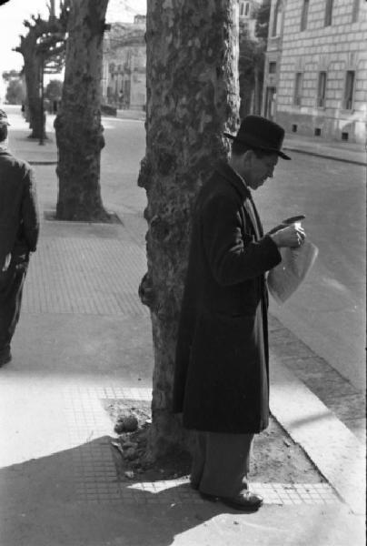 Italia Dopoguerra. Napoli. Un uomo con cappello legge un giornale lungo la strada