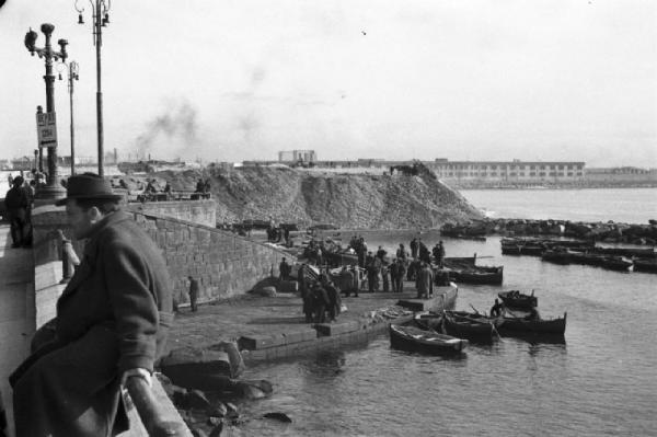 Italia Dopoguerra. Pozzuoli. Piccole imbarcazioni ormeggiate al porto. Gruppi di persone parlano lungo la banchina