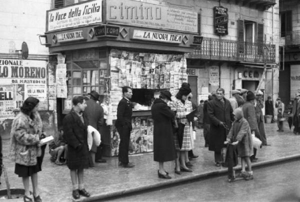 Italia Dopoguerra. Palermo. Persone in attesa su un marciapiede nei pressi di un'edicola