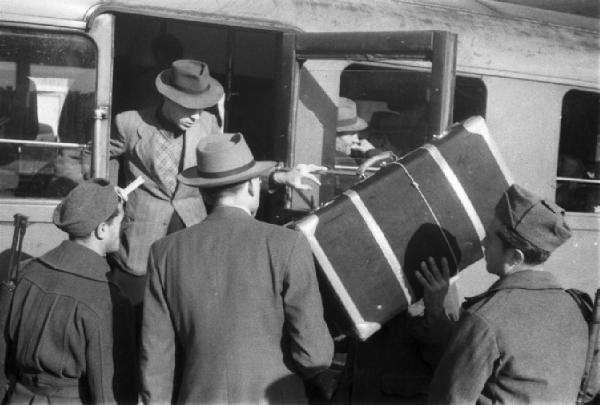 Italia Dopoguerra. Messina. Stazione ferroviaria. Un uomo scende da una littorina, un altro lo aiuta prendendo la valigia, folla di persone in attesa di salire