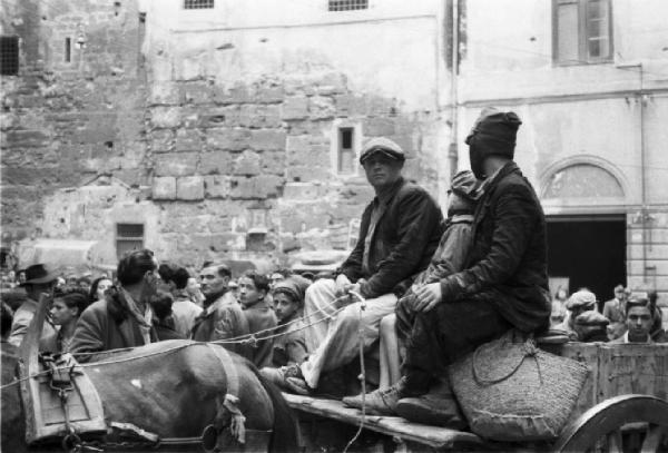 Italia Dopoguerra. Palermo. Tre persone su un carretto trainato da cavallo e folla di persone che assistono ad una danza popolare