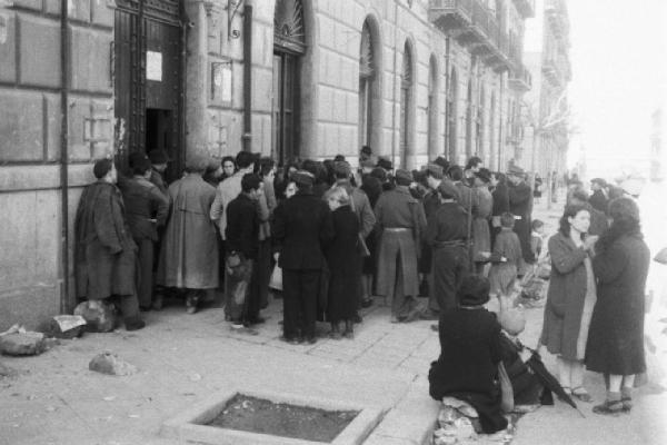 Italia Dopoguerra. Palermo. Persone in coda al'esterno di un edificio. Militari svolgono servizio d'ordine