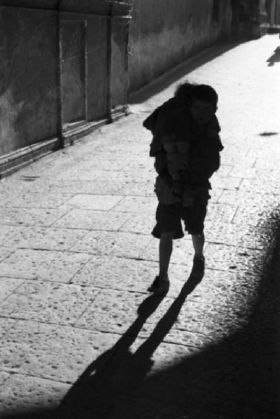 Italia Dopoguerra. Monreale. Un bamibino cammina lungo una via tenendo in braccio il fratellino piccolo