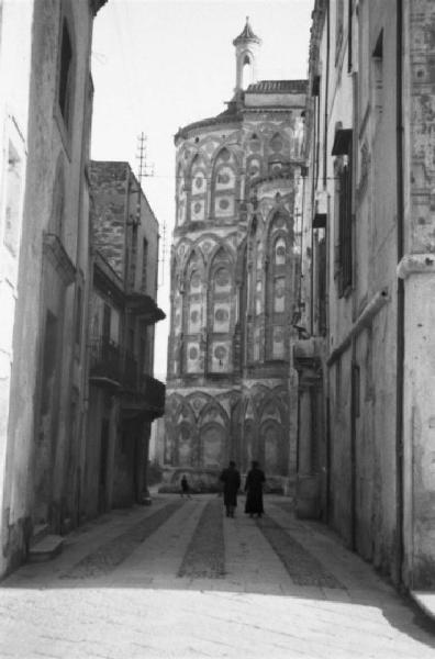 Italia Dopoguerra. Monreale. Due persone camminano lungo una via, sullo sfondo la Cattedrale