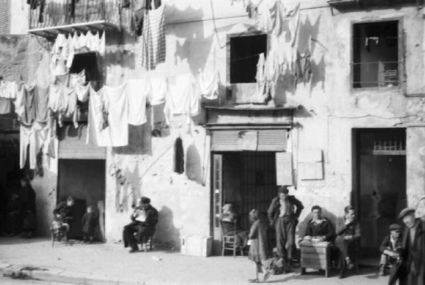 Italia Dopoguerra. Palermo. Persone sedute davanti all'uscio di negozi. Panni stesi ai balconi