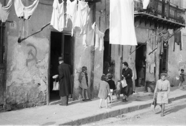 Italia Dopoguerra. Palermo. Persone sull'uscio di casa, bambini lungo la strada, panni stesi ai balconi