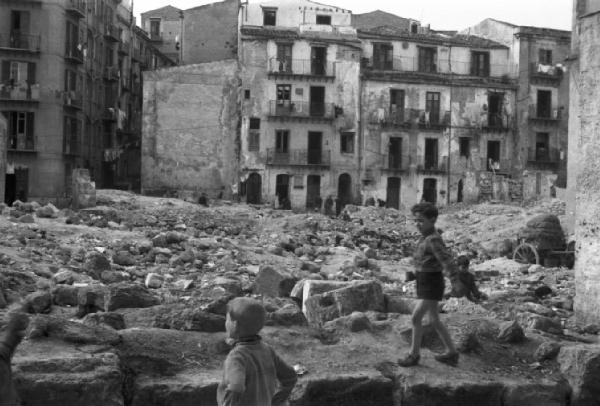 Italia Dopoguerra. Palermo. Un bambino cammina su un muretto con macerie di edifici distrutti dai bombardamenti. Abitazioni sullo sfondo