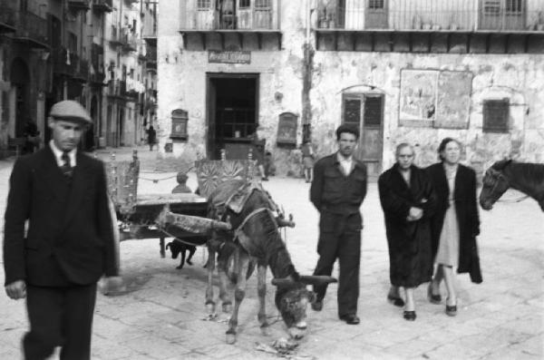 Italia Dopoguerra. Palermo. Un asino legato ad un carretto siciliano. Passanti