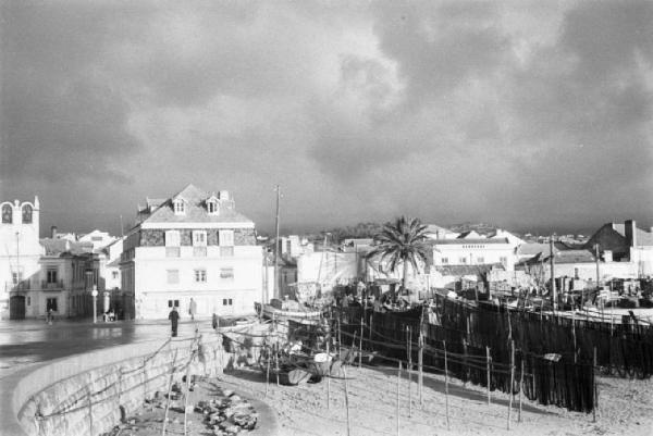 Portogallo. Cascais. Veduta della zona in riva all'oceano - spiaggia con le reti dei pescatori stese sulle palizzate  ed edifici sullo sfondo