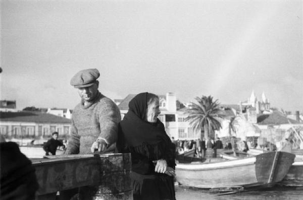 Portogallo. Cascais. Nei pressi del porto. Pescatore e anziana - sullo sfondo una piazza del paese