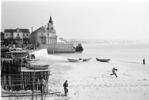Portogallo. Cascais. Spiaggia con reti dei pescatori stese ad asciugare - barche in secca - sullo sfondo edifici del paese