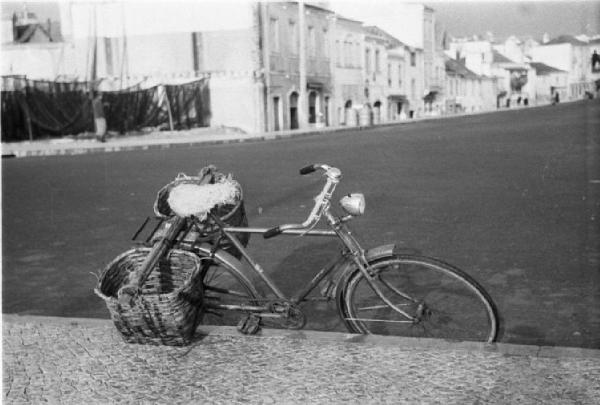 Portogallo. Cascais. Nei pressi del porto. Bicicletta con due cestini appoggiata ad un marciapiede