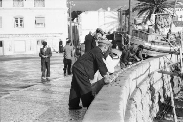 Portogallo. Cascais. Pescatori affacciati ad un muretto - sotto, le barche sulla spiaggia