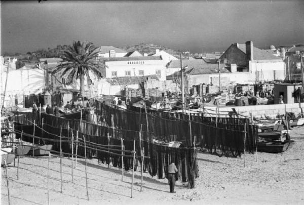 Portogallo. Cascais. Reti dei pescatori sulla spiaggia - sullo sfondo mercato del pesce ed edifici del paese