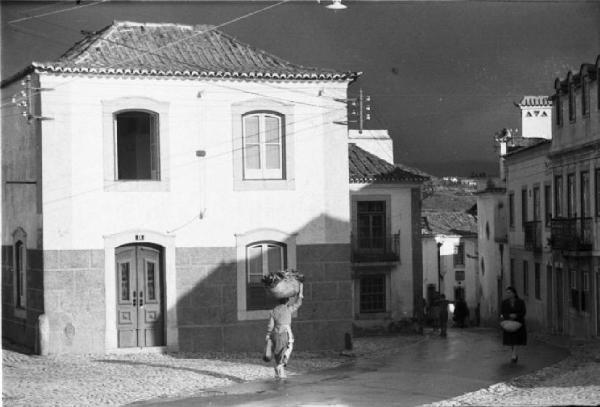 Portogallo. Cascais. Piazzetta di paese - una donna porta un cesto sulla testa