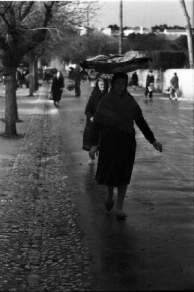 Portogallo. Cascais. Donna porta un cesto sulla testa per le vie del paese